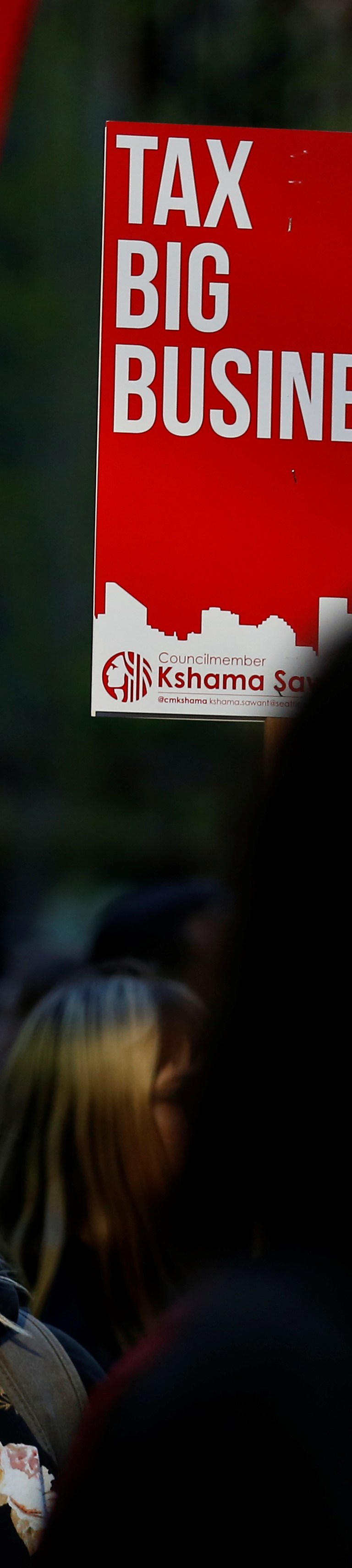 A woman holds a sign supporting the taxation of big businesses during a protest in front of the Amazon Spheres to demand that the city of Seattle tax the largest corporations to help fund affordable housing, according to organizers, in Seattle, Washington, U.S., April 10, 2018.  REUTERS/Lindsey Wasson - RC1F0EDB1690