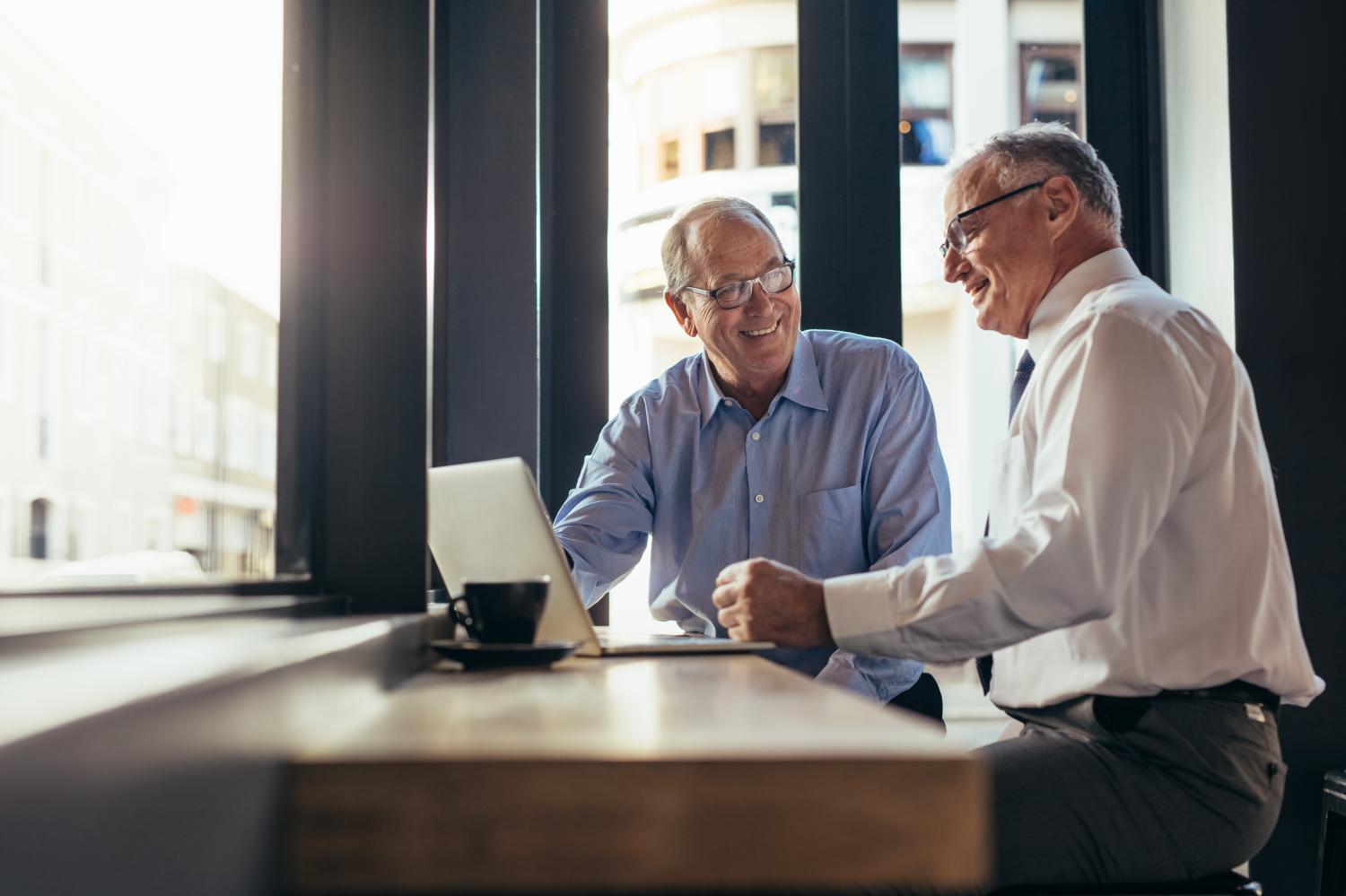 Two senior business men working together in modern cafe. Business partners sitting near window with laptop on table