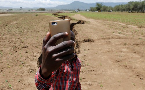 A man holds his phone to take a Facebook live video near a chasm suspected to have been caused by a heavy downpour along an underground fault-line near the Rift Valley town of Mai Mahiu, Kenya March 28, 2018. Picture taken March 28, 2018. REUTERS/Thomas Mukoya - RC12E3D4ACD0