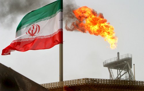A gas flare on an oil production platform in the Soroush oil fields is seen alongside an Iranian flag in the Gulf July 25, 2005. REUTERS/Raheb Homavandi/File Photo - GF10000386922