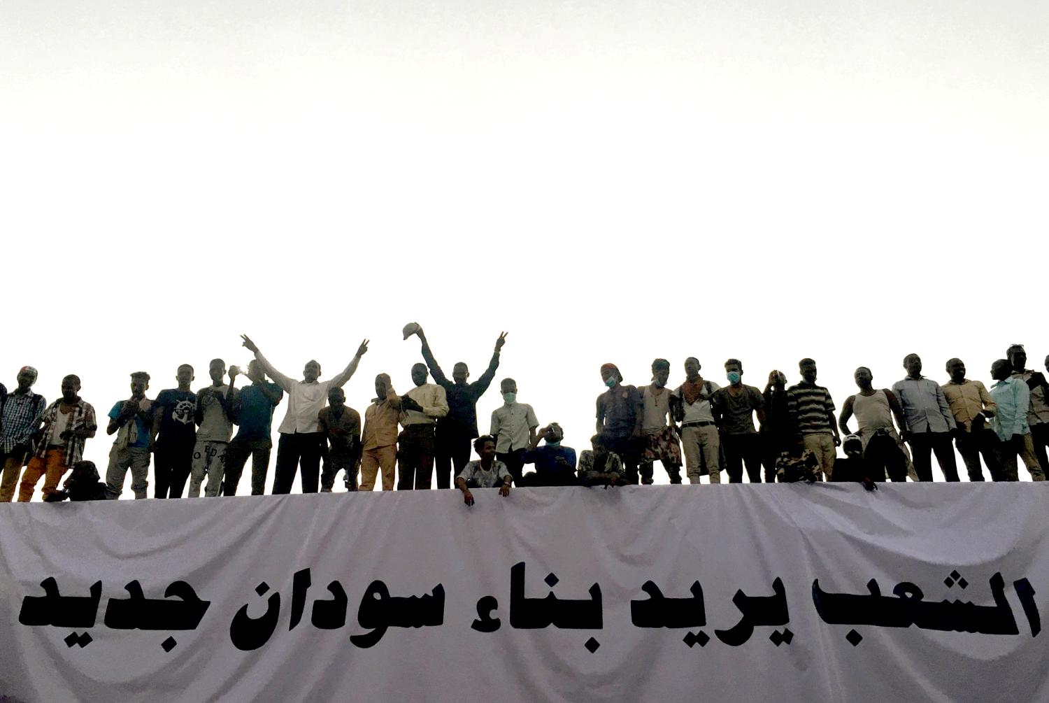 Sudanese demonstrators stand next to a banner reading in Arabic "People want to build new Sudan" as they chant slogans during a protest rally demanding Sudanese President Omar Al-Bashir to step down, outside Defence Ministry in Khartoum, Sudan April 9, 2019. REUTERS/Stringer - RC1BCDBB6200