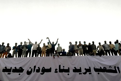 Sudanese demonstrators stand next to a banner reading in Arabic "People want to build new Sudan" as they chant slogans during a protest rally demanding Sudanese President Omar Al-Bashir to step down, outside Defence Ministry in Khartoum, Sudan April 9, 2019. REUTERS/Stringer - RC1BCDBB6200
