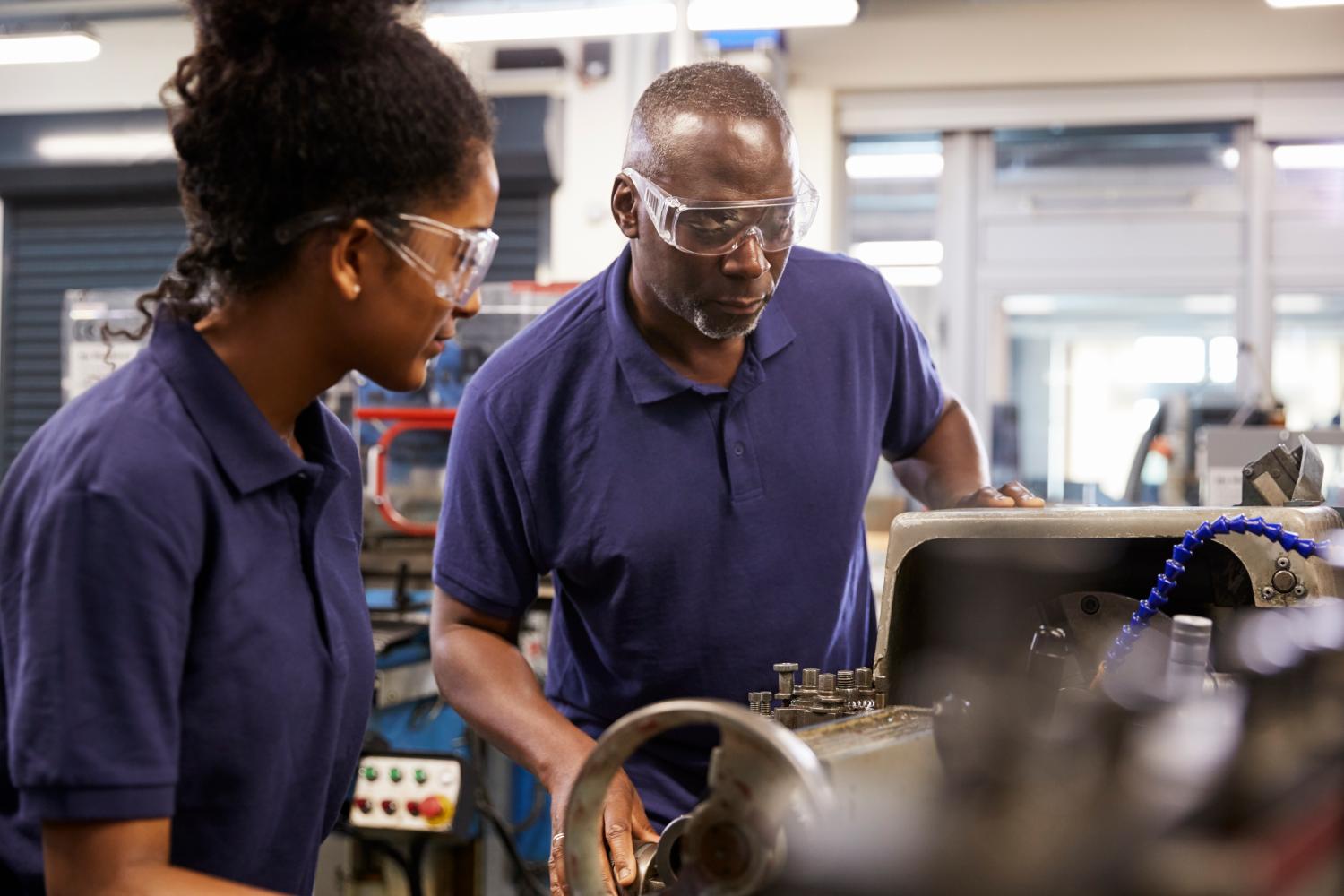 Engineer Showing Female Teenage Apprentice How To Use Lathe