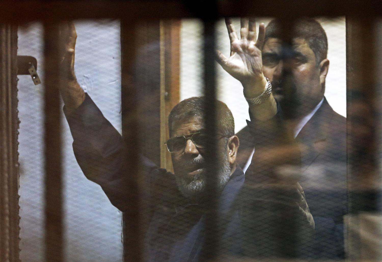 Deposed Egyptian President Mohamed Mursi greets his lawyers and people from behind bars after his verdict at a court on the outskirts of Cairo, Egypt June 16, 2015. An Egyptian court sentenced deposed President Mohamed Mursi to death on Tuesday on charges of killing, kidnapping and other offences during a 2011 mass jail break.The general guide of the Muslim Brotherhood, Mohamed Badie, and four other Brotherhood leaders were also handed the death penalty. More than 80 others were sentenced to death in absentia. REUTERS/Asmaa Waguih      TPX IMAGES OF THE DAY      - GF10000129302