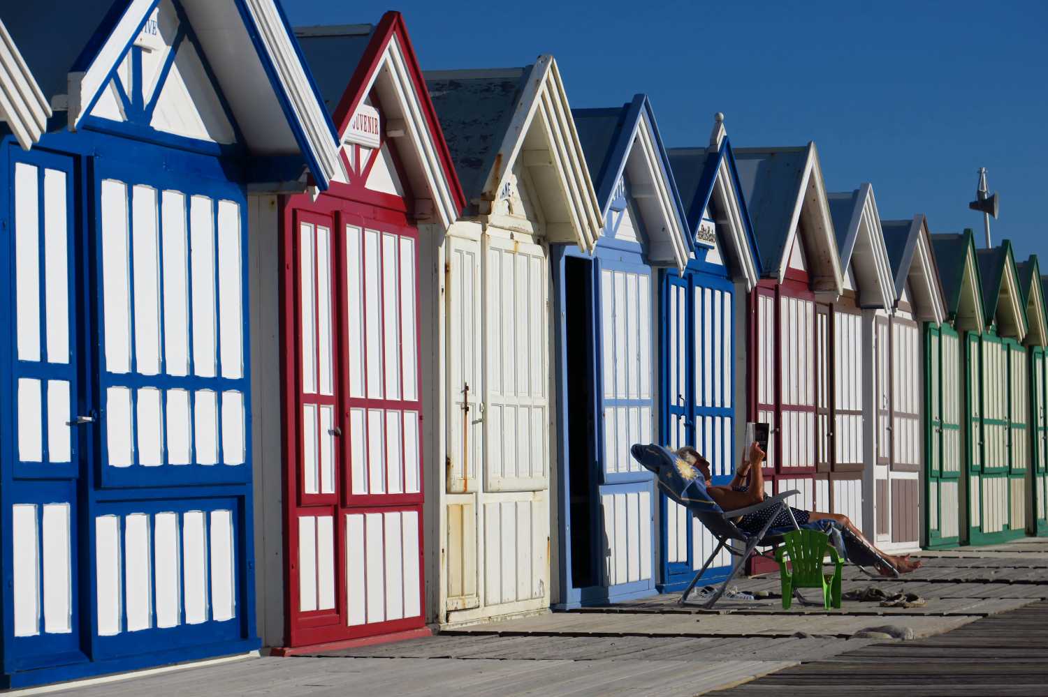 A woman reads a book in front a beach cabin on the pebbled beach in Cayeux-sur-Mer, on the North coast as sunny weather arrives in France, June 26, 2018. REUTERS/Pascal Rossignol - RC1DCF86C5D0