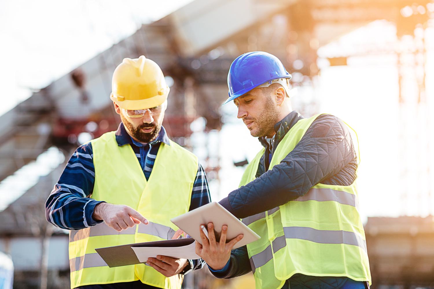 Two engineers in protective helmets and fluorescent vests showing the construction site and building activities after the successful project phase.