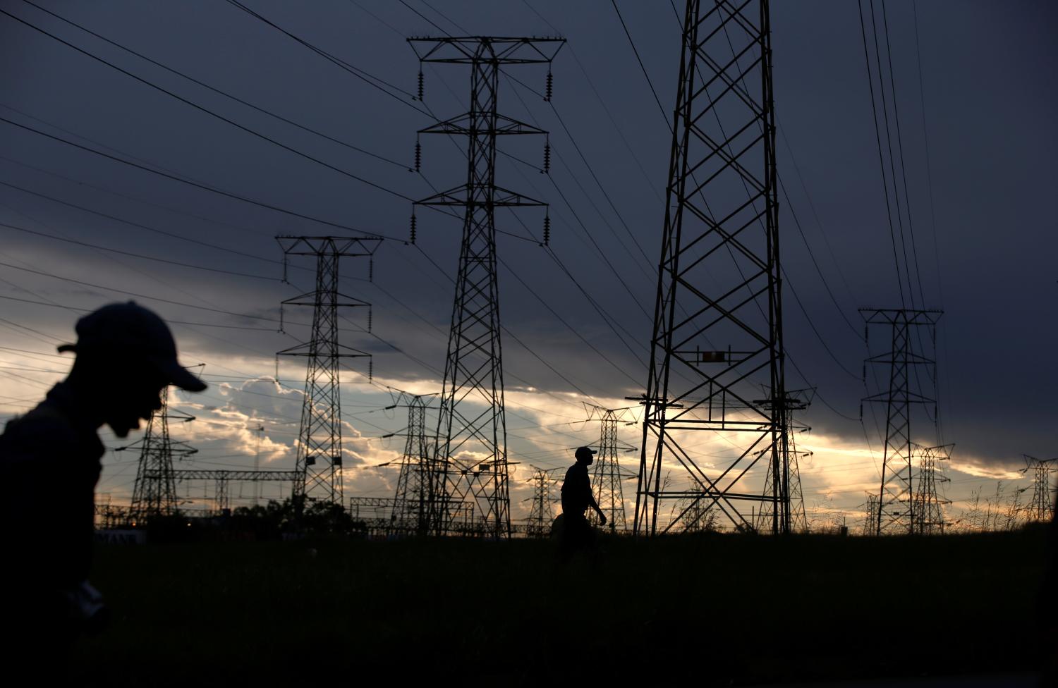 Men walk past electricity pylons as they return from work in Orlando, Soweto township, South Africa March 18, 2019. REUTERS/Siphiwe Sibeko - RC1C1FC73920
