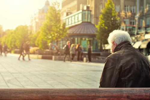 older man sits on a bench in a city square