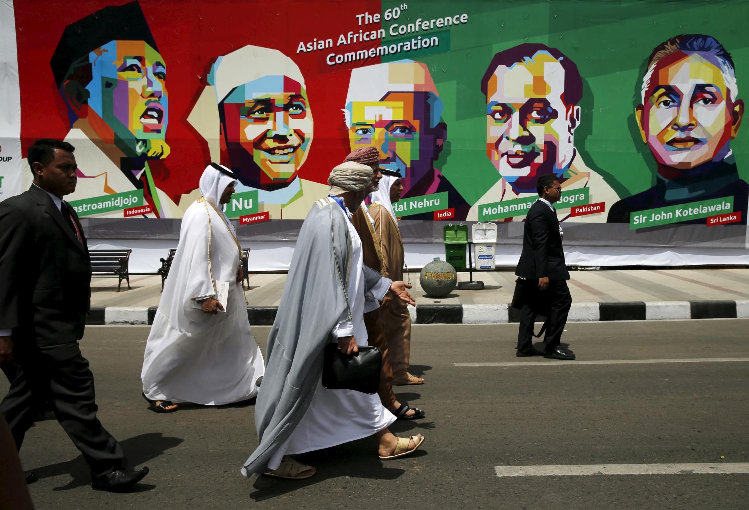 Delegates walk in front a poster of prominent attendees of the 1955 Asian-African Conference during a historical walk commemorating the 60-year anniversary of the Asian-African Summit, on Asia Afrika street in Bandung, Indonesia April 24, 2015. Leaders of Asian and African nations are in Jakarta to mark the 60th anniversary of a conference that made a developing-world stand against colonialism and led to the Cold War era's non-aligned movement.