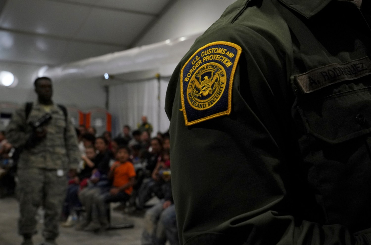 A Customs and Border Patrol officer stands near migrants at the Donna Soft-Sided Processing Facility in Donna, Texas, U.S. July 12, 2019. Picture taken July 12, 2019. REUTERS/Veronica G. Cardenas - RC15F00ADDE0