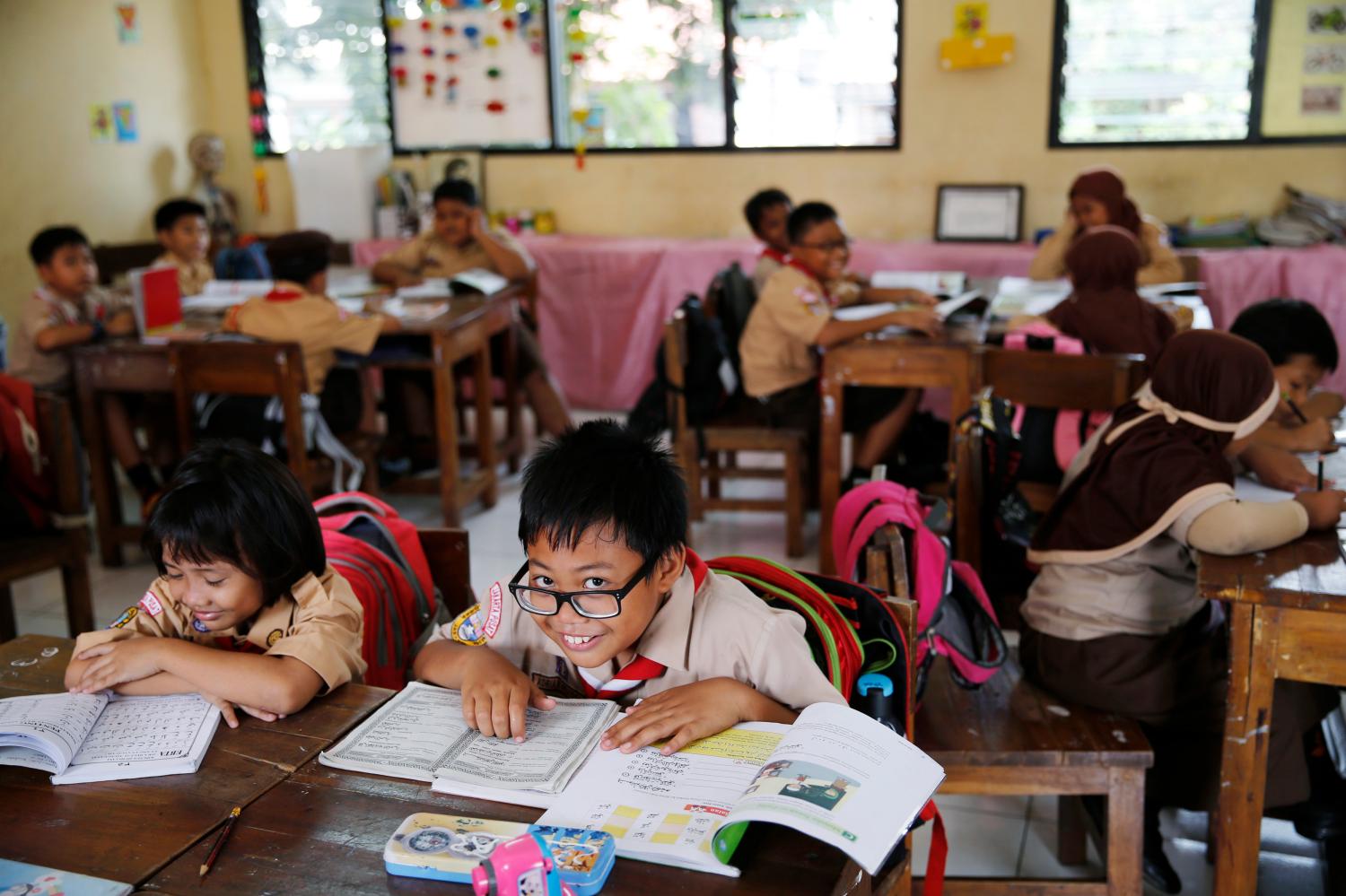 A student reacts to the camera as a teacher teaches the 2013 curriculum inside a classroom at Cempaka Putih district in Jakarta, October 15, 2014. Indonesia plans to discontinue early next year the widely criticised school curriculum that emphasises moral and religious education, a minister said on Monday. Picture taken October 15, 2014. REUTERS/Beawiharta (INDONESIA - Tags: EDUCATION POLITICS) - GM1EAC81NZV01