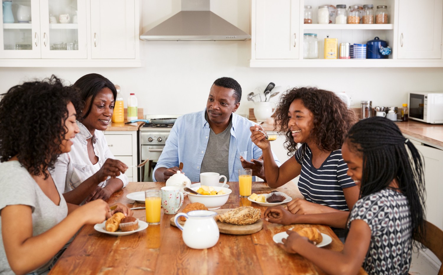 Family Using Gadgets Whilst Eating Breakfast Together In Kitchen