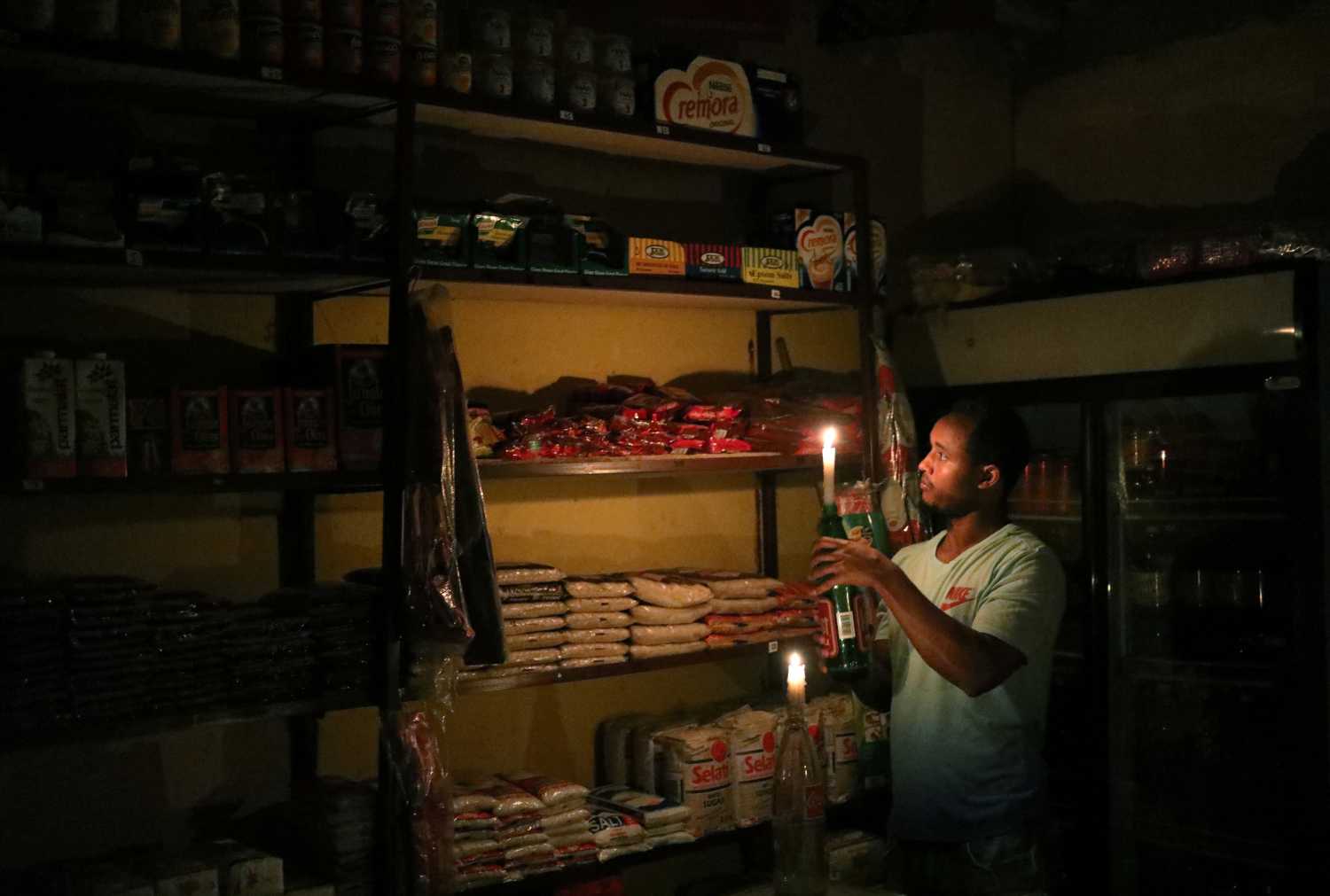 Mulugeta Desalegn, an owner of a convenience store, or "spaza shop", picks an item for a customer as he holds a candle, in Senaone, Soweto, South Africa March 18, 2019. REUTERS/Siphiwe Sibeko - RC13FB1CC910