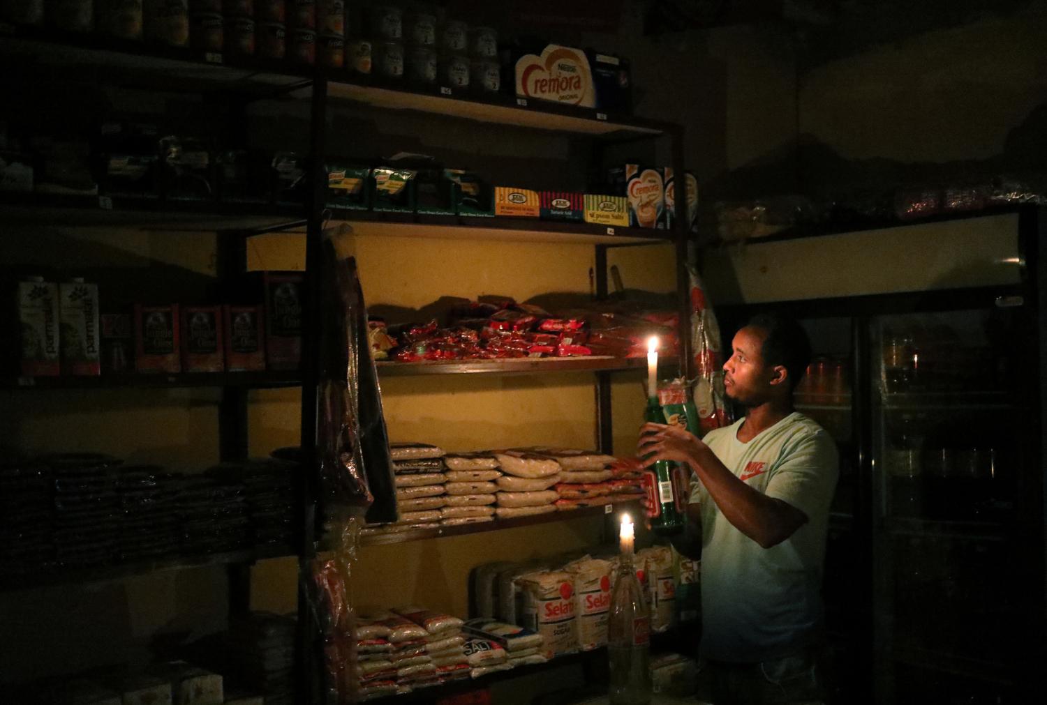 Mulugeta Desalegn, an owner of a convenience store, or "spaza shop", picks an item for a customer as he holds a candle, in Senaone, Soweto, South Africa March 18, 2019. REUTERS/Siphiwe Sibeko - RC13FB1CC910