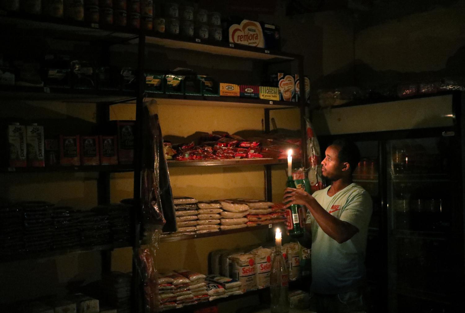 Mulugeta Desalegn, an owner of a convenience store, or "spaza shop", picks an item for a customer as he holds a candle, in Senaone, Soweto, South Africa March 18, 2019. REUTERS/Siphiwe Sibeko - RC13FB1CC910