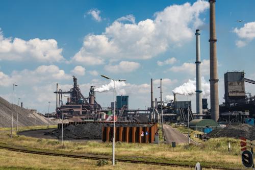 Steel mill with smoking chimneys and heaps of raw material located on the Dutch coast during a cloudy day. Thick smoke is coming from the cimneys.