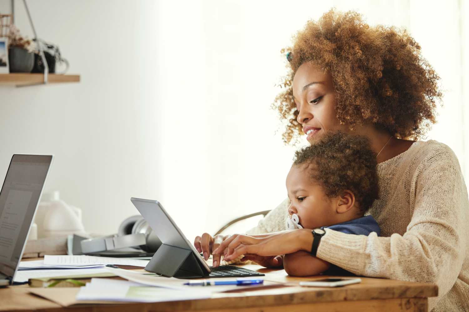 Woman typing on digital taMother using wireless computer while holding son at table.