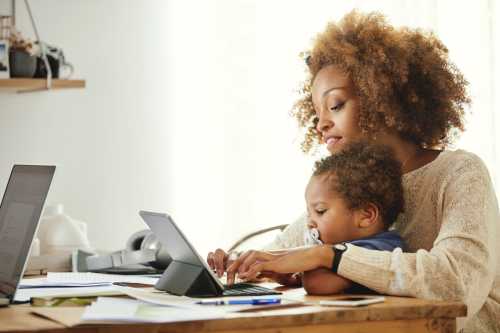 Woman typing on digital taMother using wireless computer while holding son at table.