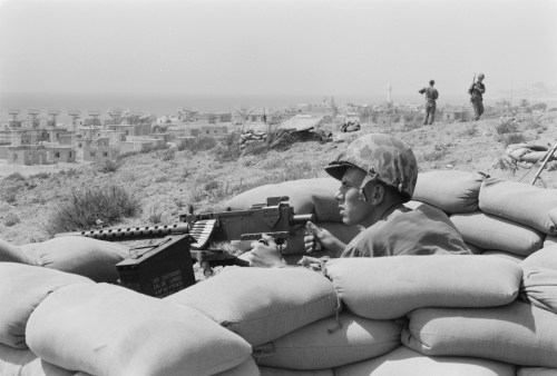 U.S. Marine sits in a foxhole and points a machine gun towards Beirut, Lebanon, in the distance