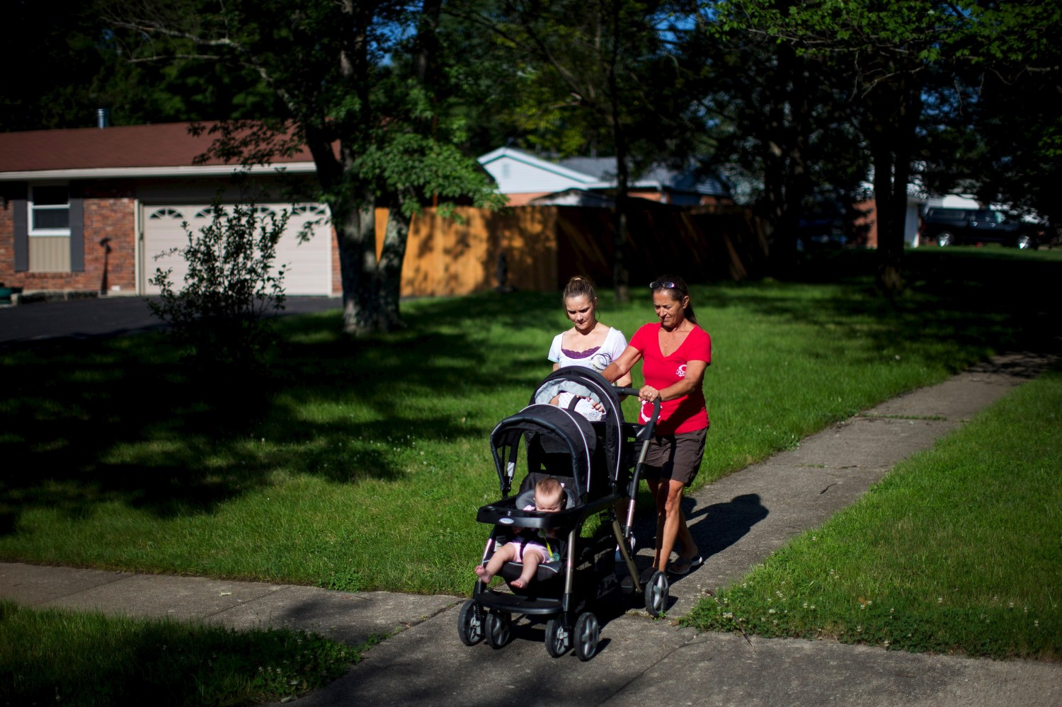 Heather Padgett, with her mother Debi Padgett (R), takes her daughters Kinsley and Kiley for a walk outside their home in Cincinnati, Ohio July 16, 2015. Until she got clean last August, Heather was part of what the Centers for Disease Control has called a heroin epidemic - a 100 percent rise in heroin addiction among Americans between 2002 and 2013. The sharp rise in heroin addiction, coupled with the risks of newborns developing withdrawal symptoms after they are sent home, has led a group of Cincinnati hospitals to try what they say is the first program of its kind in the United States: testing all mothers, or their infants, for opiates regardless of background, not just those who seem high-risk. To match Feature USA-HEROIN/MATERNALTESTING  Picture taken July 16, 2015.  REUTERS/Aaron P. Bernstein - GF20000015645