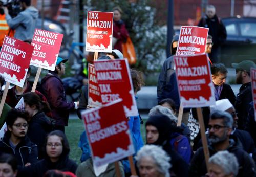 People hold "tax Amazon" signs during a protest in front of the Amazon Spheres to demand that the city of Seattle tax the largest corporations to help fund affordable housing, according to organizers, in Seattle, Washington, U.S., April 10, 2018.  REUTERS/Lindsey Wasson - RC1D126DE1E0