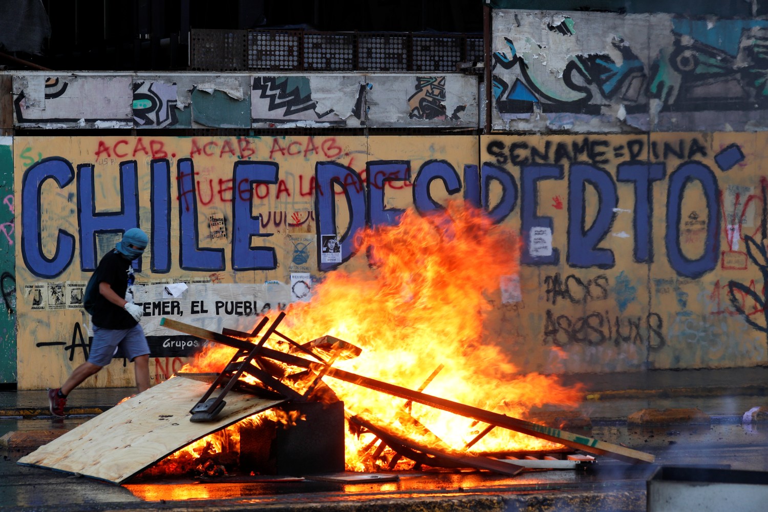 A demonstrator walks past a burning barricade during a protest against Chile's government in Santiago, Chile October 30, 2019. The graffiti on the wall reads: "Chile woke up". REUTERS/Jorge Silva - RC1AFD58CC70