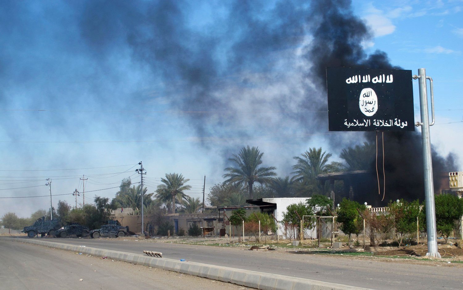 Smoke raises behind an Islamic State flag after Iraqi security forces and Shiite fighters took control of Saadiya in Diyala province from Islamist State militants, November 24, 2014. Iraqi forces said on Sunday they retook two towns north of Baghdad from Islamic State fighters, driving them from strongholds they had held for months and clearing a main road from the capital to Iran. There was no independent confirmation that the army, Shi'ite militia and Kurdish peshmerga forces had completely retaken Jalawla and Saadiya, about 115 km (70 miles) northeast of Baghdad. Many residents fled the violence long ago. At least 23 peshmerga and militia fighters were killed and dozens were wounded in Sunday's fighting, medical and army sources said.  REUTERS/Stringer (IRAQ - Tags: CIVIL UNREST CONFLICT MILITARY TPX IMAGES OF THE DAY) - GM1EABP0BT301