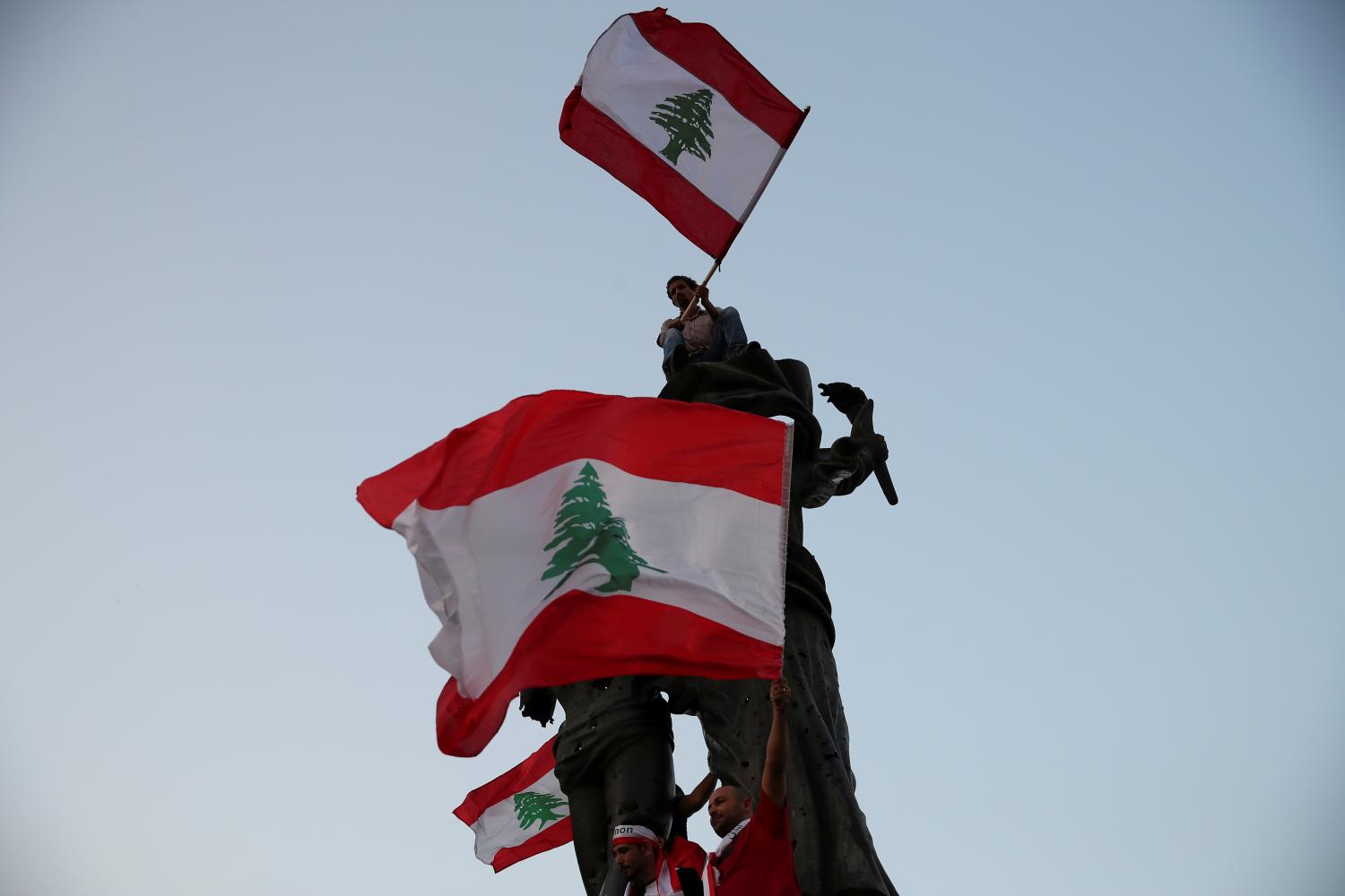 Demonstrators wave Lebanese national flags as they stand atop a statue on Martyrs' square during an anti-government protest in downtown Beirut, Lebanon October 22, 2019. REUTERS/Alkis Konstantinidis - RC1AE78FCA00