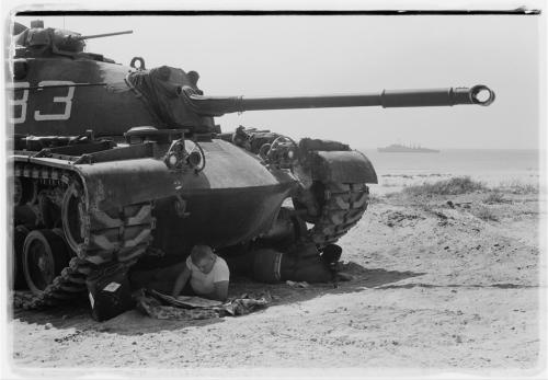 American soldier reads a newspaper in the shade under a U.S. Marine tank in Beirut, Lebanon. / Library of Congress