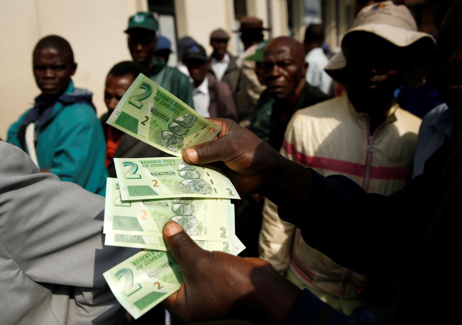 A man poses with Zimbabwe's new two dollar banknotes as customers queue outside a bank in Harare, Zimbabwe, November 12, 2019. REUTERS/Philimon Bulawayo - RC2J9D9ID88X
