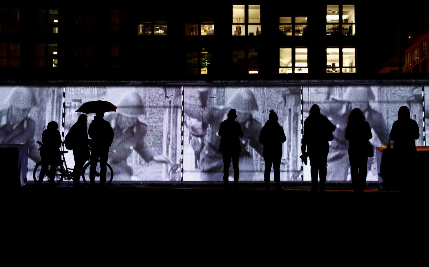 People stand in front of a projection on the East Side Gallery, the largest remaining part of the former Berlin Wall, in Berlin, Germany, November 4, 2019. On November 9th Germany will mark the 30th anniversary of the fall of the Berlin Wall (Berliner Mauer) in 1989. REUTERS/Fabrizio Bensch - RC1D9112CB30