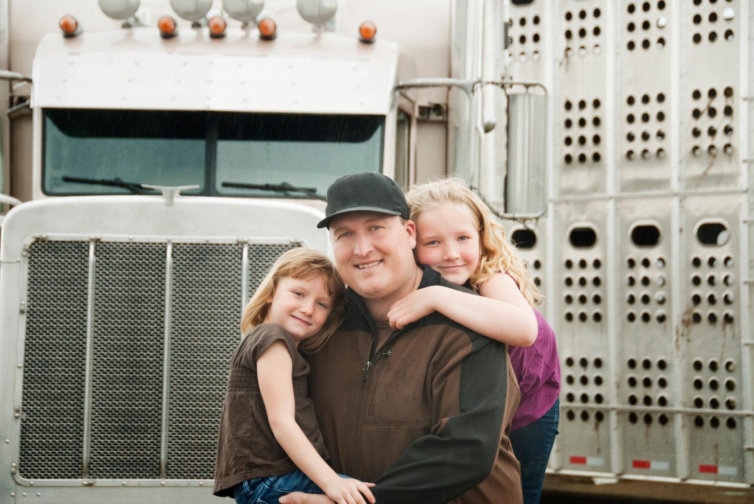 Cattle hauler truck driver and his daughters standing in front of his truck. It is raining.