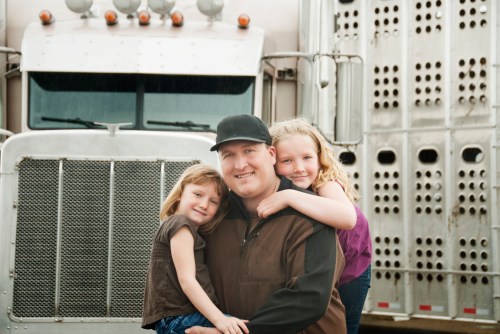 Cattle hauler truck driver and his daughters standing in front of his truck. It is raining.