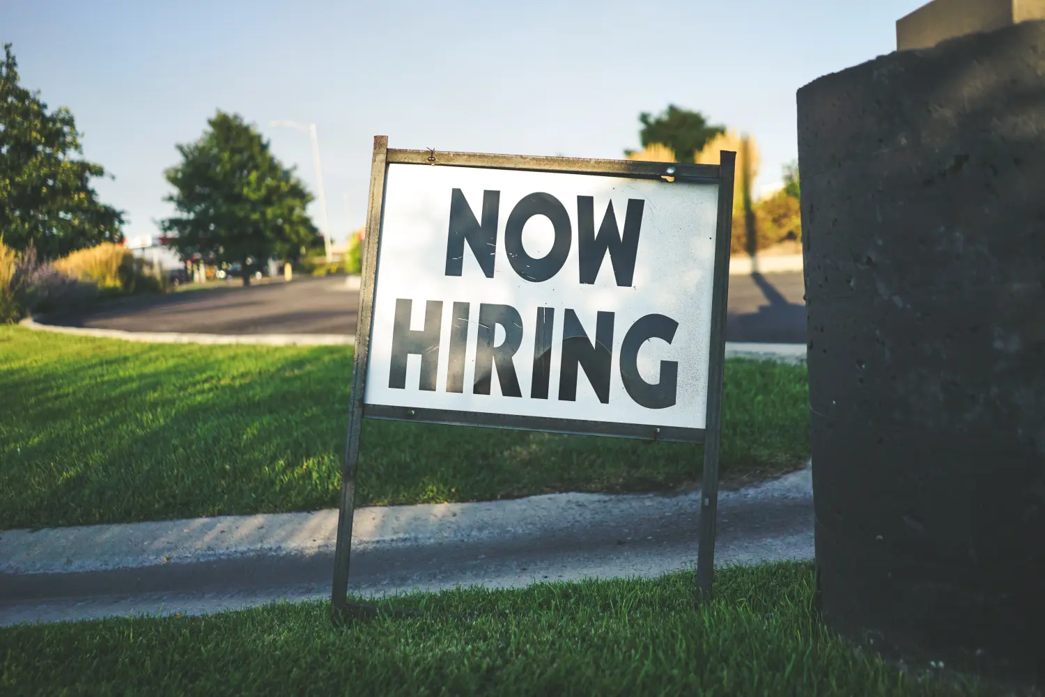 A "Now Hiring" sign stands outside a business.