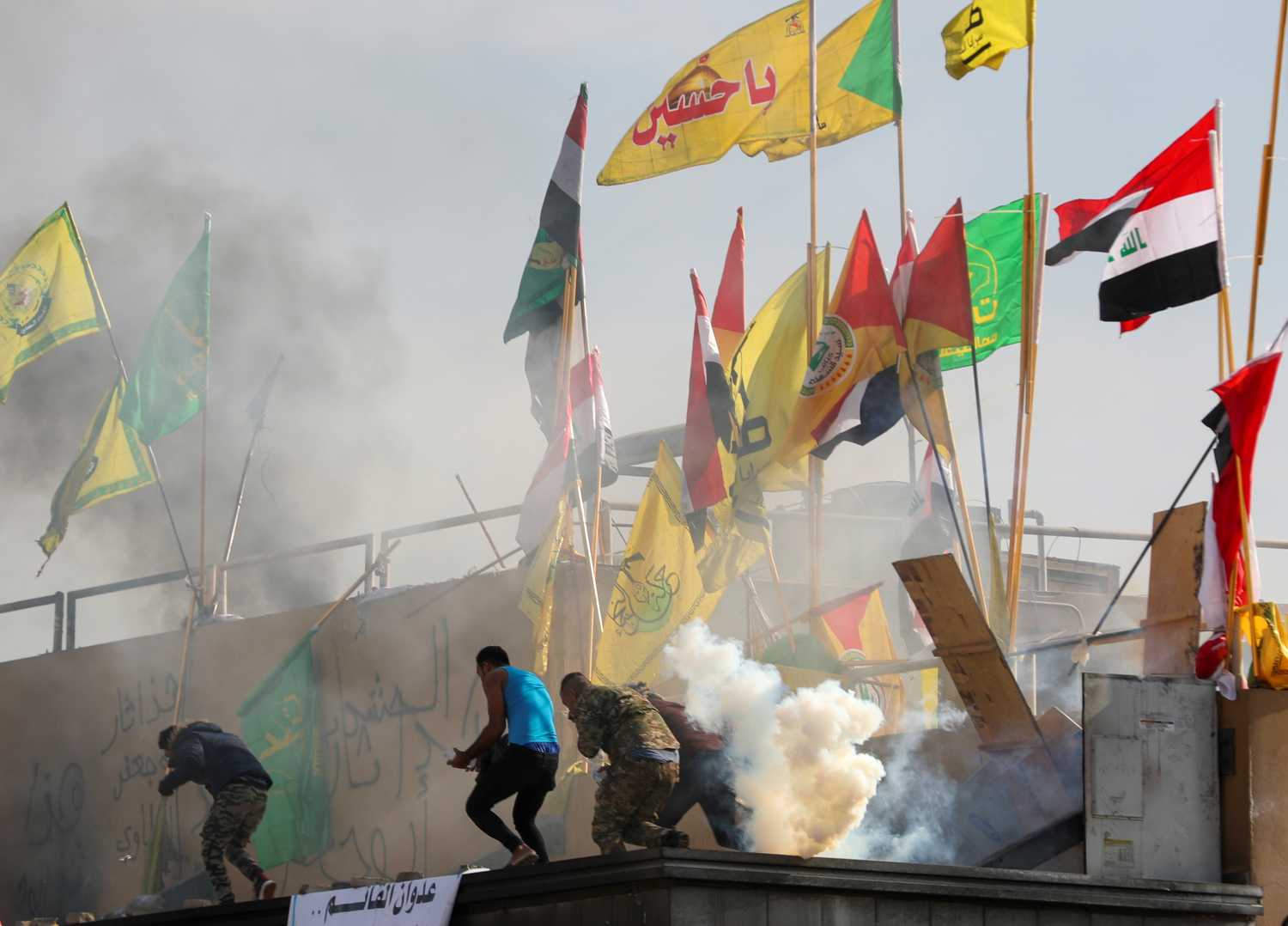 Protesters and militia fighters run away from tear gas thrown by U.S. Embassy security men, during a protest to condemn air strikes on bases belonging to Hashd al-Shaabi (paramilitary forces), outside the embassy in Baghdad, Iraq January 1, 2020. REUTERS/Thaier al-Sudani