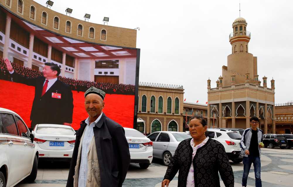 Ethnic Uighur people walk in front of a giant screen with a picture of Chinese President Xi Jinping in the main city square in Kashgar in Xinjiang Uighur Autonomous Region, China September 6, 2018. The screen broadcasts a slideshow of images of Xi on loop, including propaganda images of his previous visit to Xinjiang. Picture taken September 6, 2018. To match Special Report MUSLIMS-CAMPS/CHINA REUTERS/Thomas Peter - RC1DD356DCF0