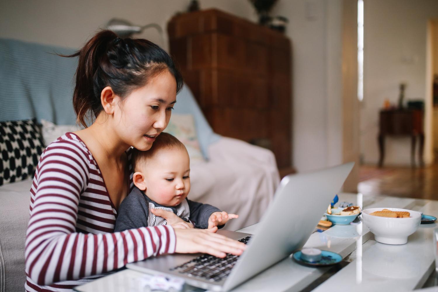 Portrait of a young Asian woman sitting at home, doing some freelance job while taking care of her little baby boy. Home living and lifestyle concepts with Asian people.