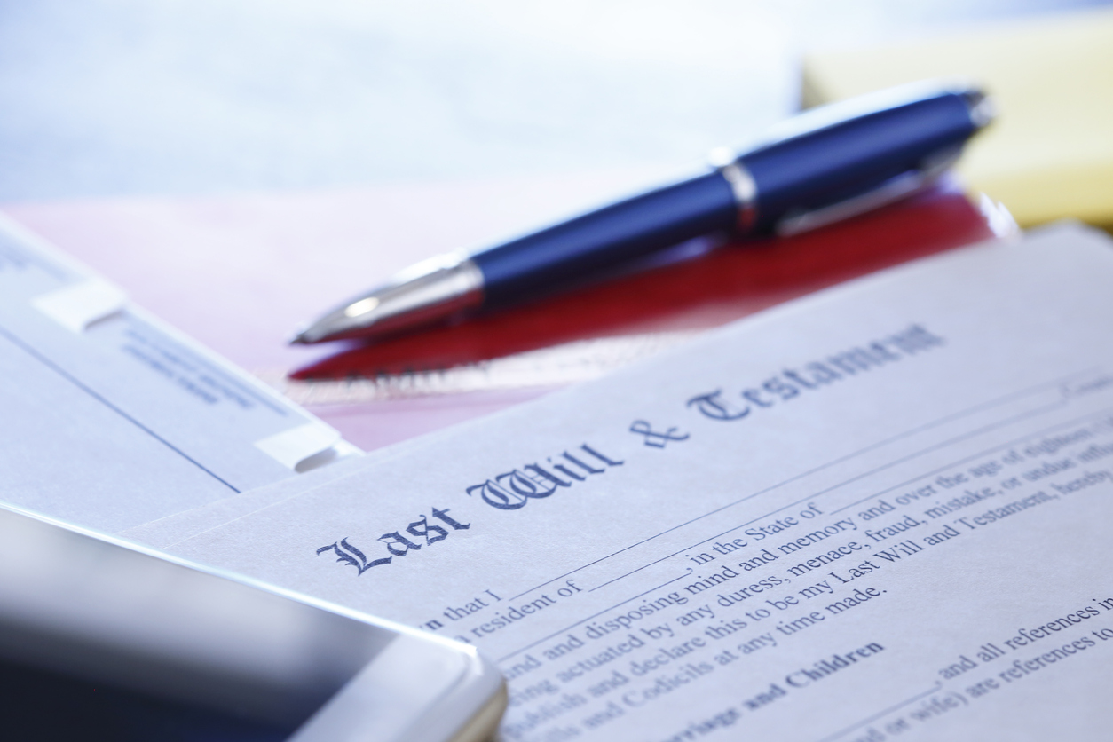 A ballpoint pen and a mobile phone rest on top of a last will and testament document that is part of the estate planning process.  This image is photographed using a very shallow depth of field.