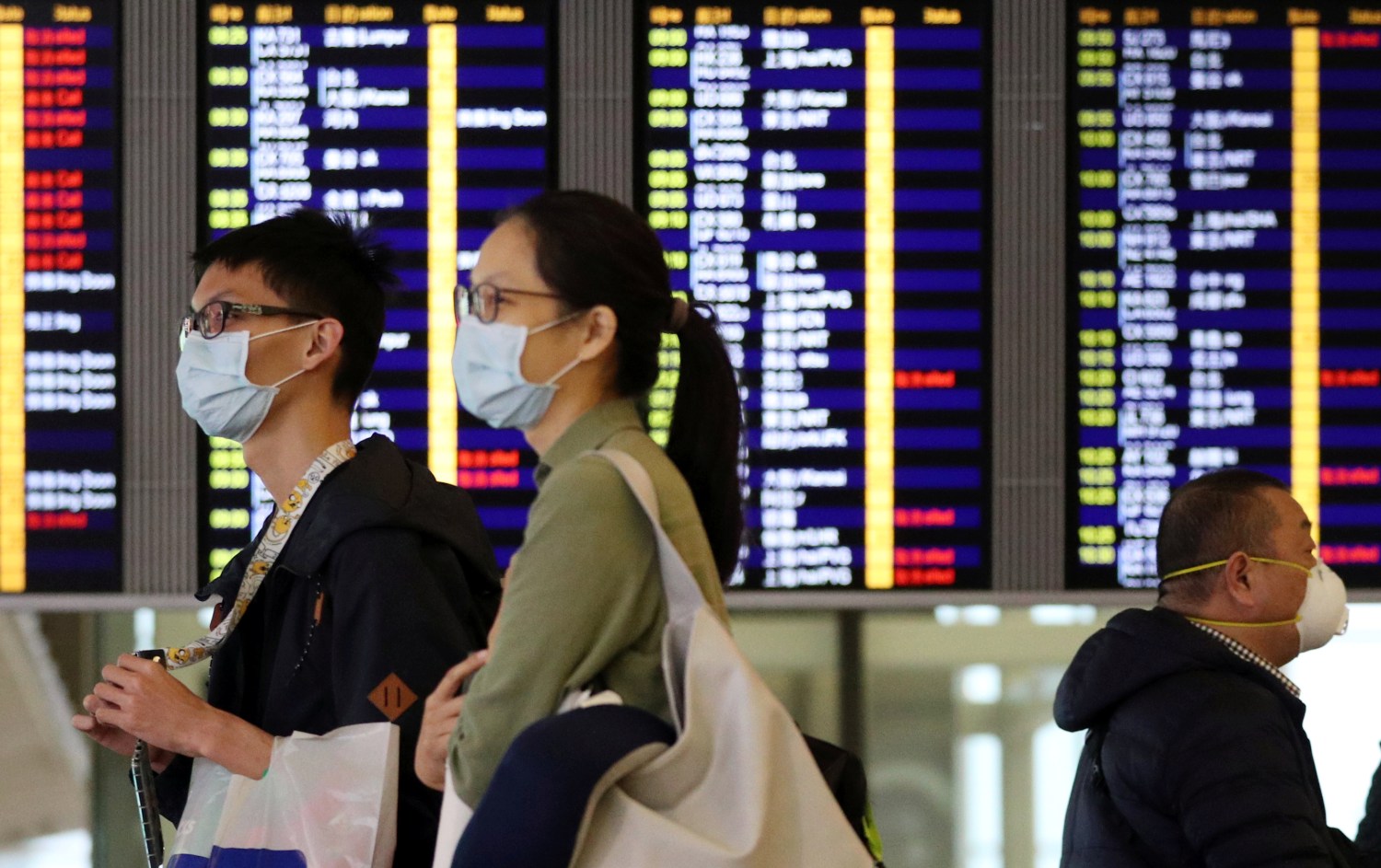 Passengers wear protective masks as they walk past an information board at Hong Kong International Airport, following the coronavirus outbreak in Hong Kong, China,