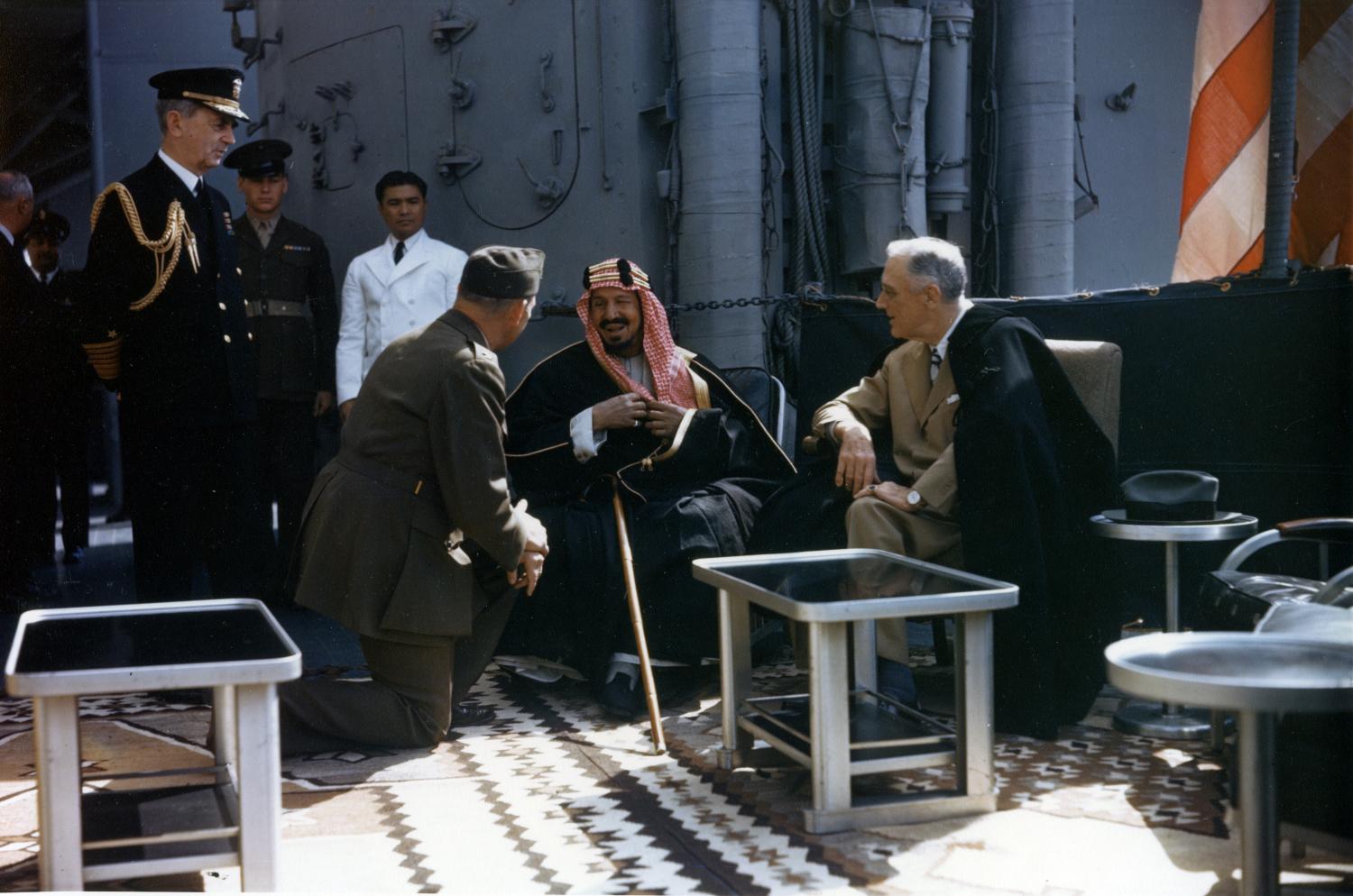 (right)  Meets with King Ibn Saud, of Saudi Arabia, on board USS Quincy (CA-71) in the Great Bitter Lake, Egypt, on 14 February 1945. The King is speaking to the interpreter, Colonel William A. Eddy, USMC. Fleet Admiral William D. Leahy, USN, the President's Aide and Chief of Staff, is at left. Note ornate carpet on the ship's deck, and life raft mounted on the side of the 5/38 twin gun mount in the background.  Photograph from the Army Signal Corps Collection in the U.S. National Archives.