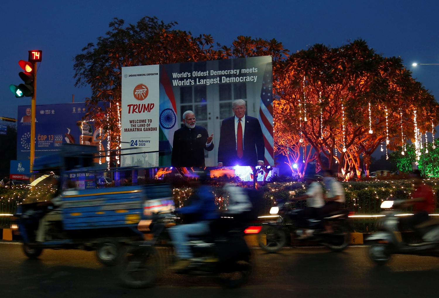 People ride their motorbikes past a hoarding with the images of India's Prime Minister Narendra Modi and U.S. President Donald Trump installed next to decorated trees alongside a road ahead of Trump's visit, in Ahmedabad, India, February 20, 2020. REUTERS/Amit Dave