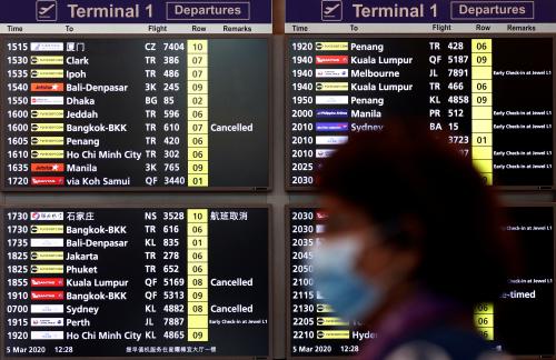 A woman wearing a mask passes a flight information board at Changi Airport in Singapore March 5, 2020. REUTERS/Edgar Su