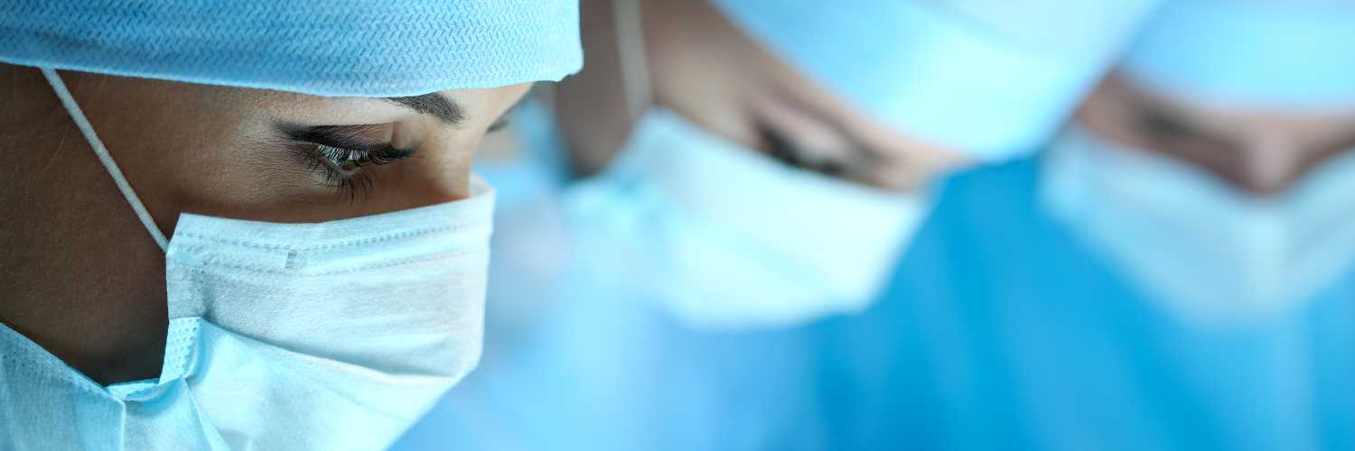 Three surgeons at work operating in surgical theatre. Resuscitation medicine team wearing protective masks saving patient. Surgery and emergency concept. Letterbox view