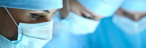 Three surgeons at work operating in surgical theatre. Resuscitation medicine team wearing protective masks saving patient. Surgery and emergency concept. Letterbox view