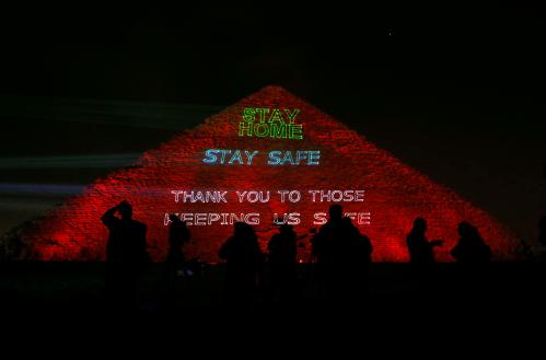 People are seen in front of the pyramid of Khufu, the largest of the Giza pyramid complex, illuminated with text encouraging to stay home, as Egypt ramps up its efforts to slow down the spread of coronavirus disease (COVID-19) outbreak, in Giza, on the outskirts of Cairo, Egypt, March 30, 2020. REUTERS/Mohamed Abd El Ghany