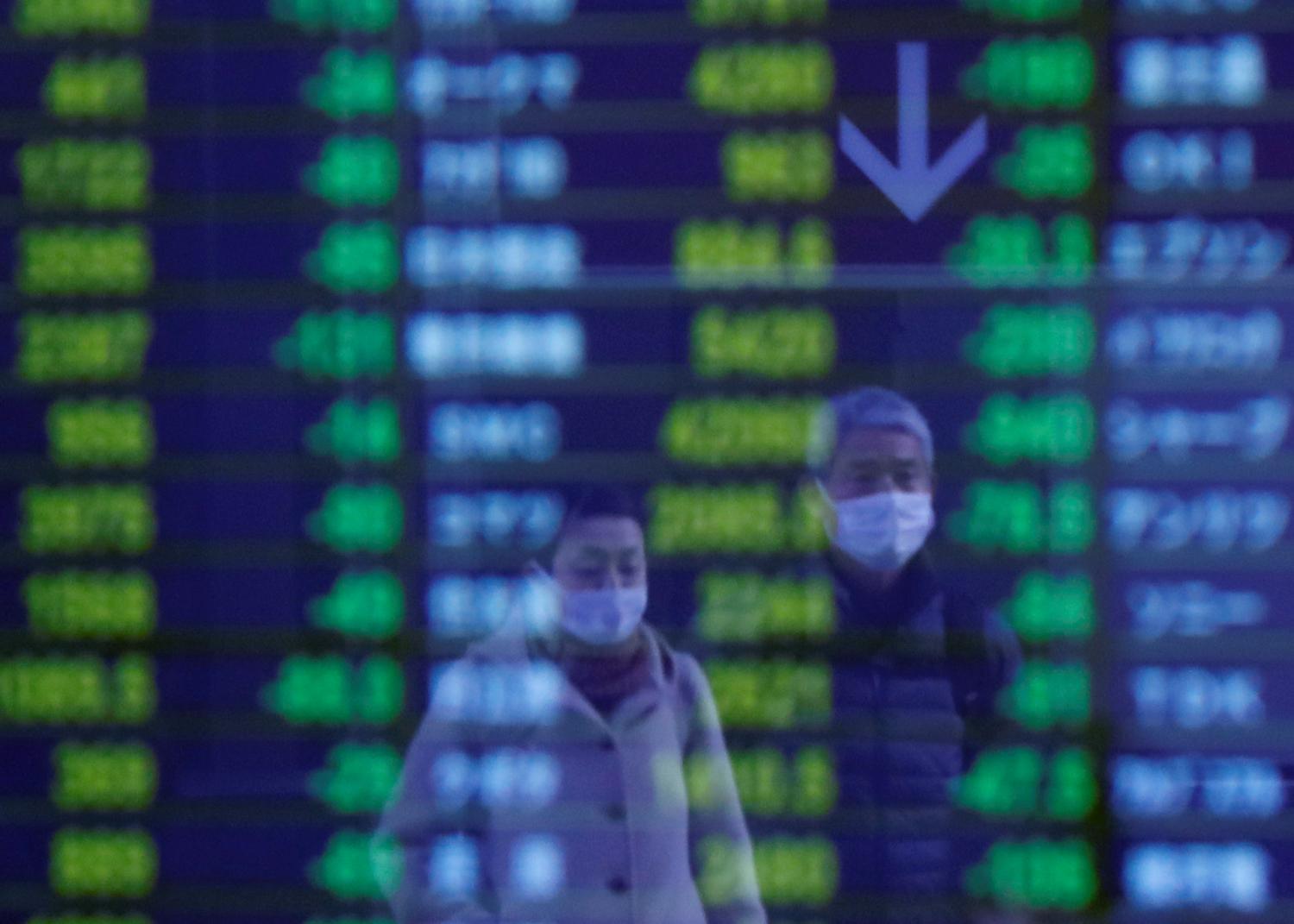 Passersby wearing protective face masks, following an outbreak of the coronavirus, are reflected on a screen displaying stock prices outside a brokerage in Tokyo, Japan March 6, 2020.   REUTERS/Issei Kato