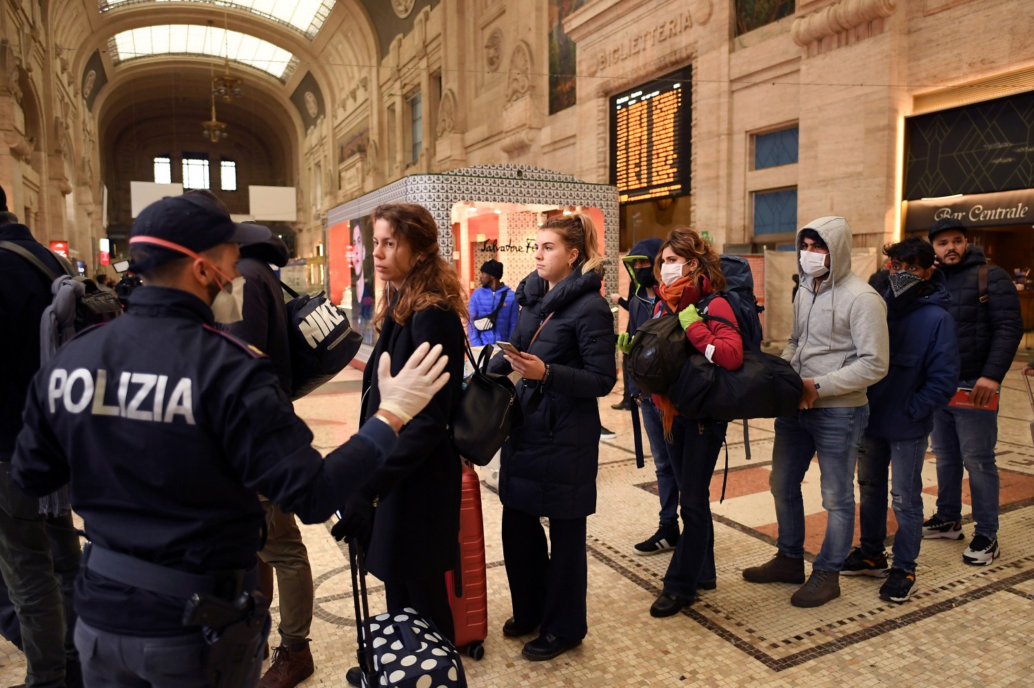 A police officer talks to people at Milan's main train station, following a government decree that has shut down large areas in the north of the country, to stem coronavirus contagion, Milan, Italy March 9, 2020. REUTERS/Daniele Mascolo