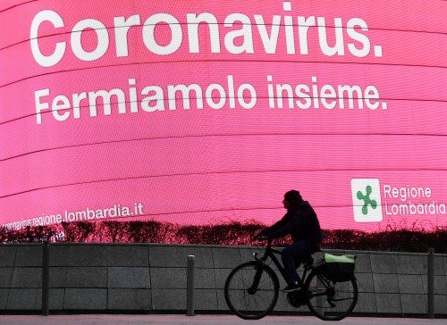 A person rides a bicycle in Piazza Gae Aulenti, on the third day of an unprecedented lockdown across of all Italy imposed to slow the outbreak of coronavirus, in Milan, Italy, March 12, 2020. The illuminated sign reads: "Coronavirus. Let's stop it together." REUTERS/Flavio Lo Scalzo