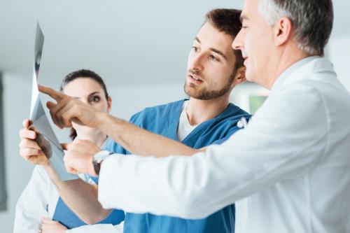 Professional medical team with doctors and surgeon examining patient's x-ray image, discussing and pointing