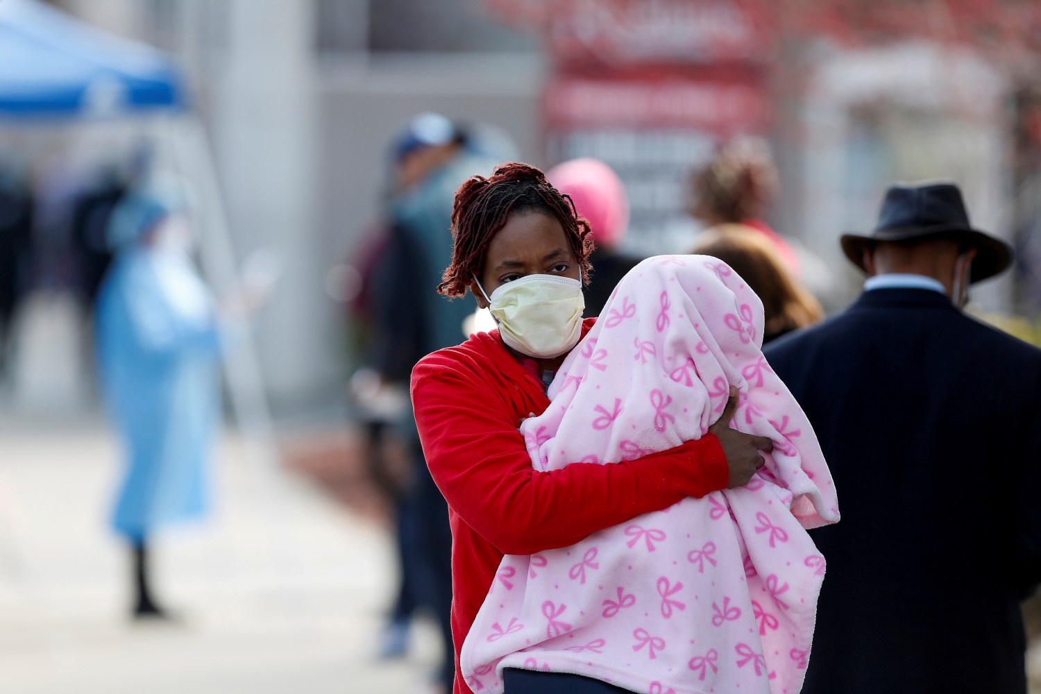 A woman holds a child as she walks past people waiting in line to receive testing during the global outbreak of the coronavirus disease (COVID-19) outside Roseland Community Hospital in Chicago, Illinois, U.S., April 7, 2020. REUTERS/Joshua Lott     TPX IMAGES OF THE DAY